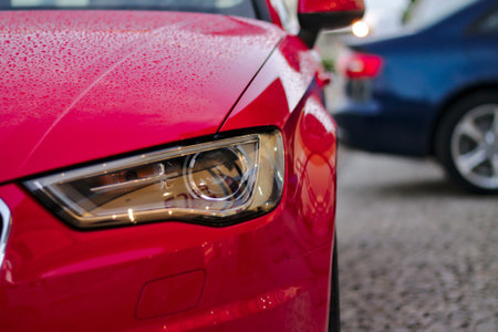 Close up of red car headlight with reflection on asphalt road.