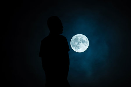 Silhouette of a man standing in front of the full moon at nightの写真素材