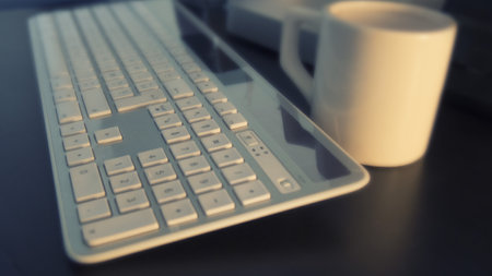 Close up of a computer keyboard and coffee cup on a desk.の写真素材