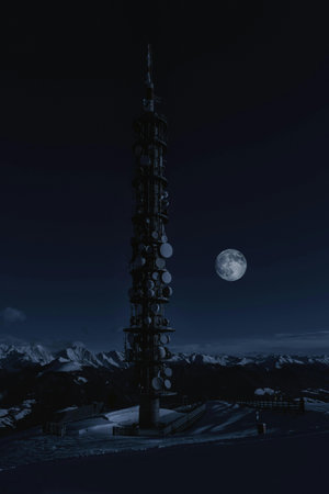 Telecommunication tower in the mountains at night with full moon in winter