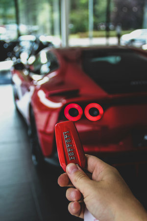 Hand holding red car key with red car in the background, car rental concept
