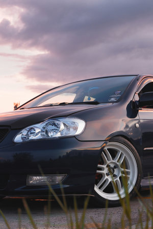 Front view of a black car in the sunset with a cloudy sky