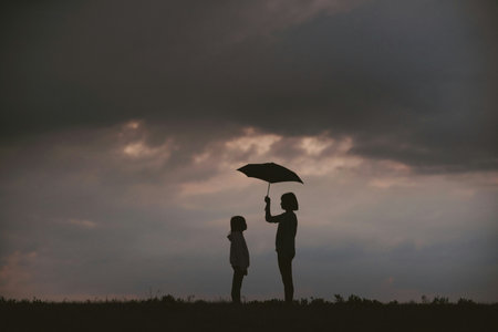 Silhouette of mother and daughter with umbrella in the field.の写真素材