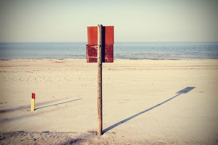 Retro filtered rusty board sign on wooden post on a beach.の写真素材