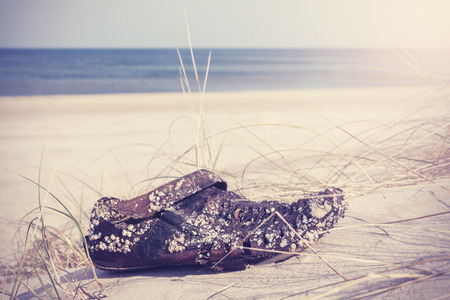 Retro filtered photo of an old weathered shoe washed up on beach.