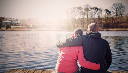 Retro filtered photo of a couple sitting on wooden pier by lake.の写真素材