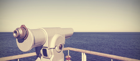 Retro vintage toned photo of a telescope on a pier pointed at horizon, future concept.の写真素材