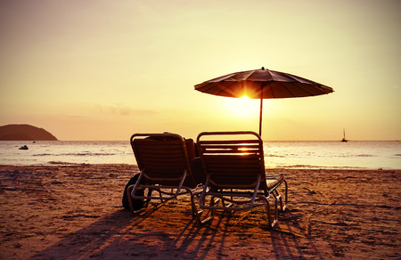Vintage instagram stylized beach chairs and umbrella at sunset. Concept for holidays and relaxation.の写真素材