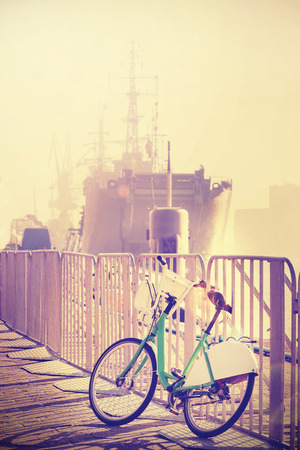 Vintage toned bicycle parked by pier with ship in a distance, sunset lens flare effect.の写真素材