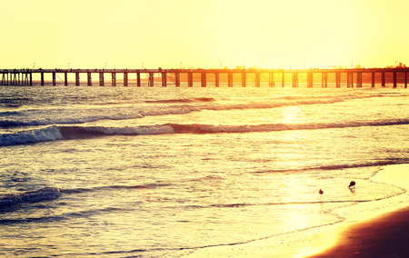 Vintage toned wooden pier on beach at sunset, California, USA.の写真素材