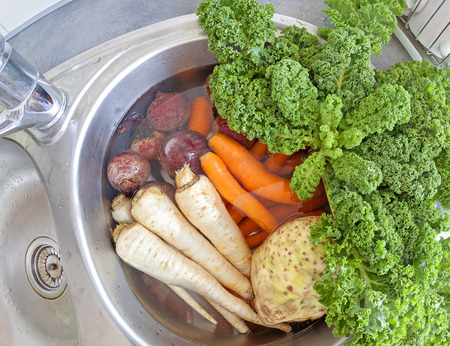 Dirty vegetables in a kitchen sink filled with water.の写真素材