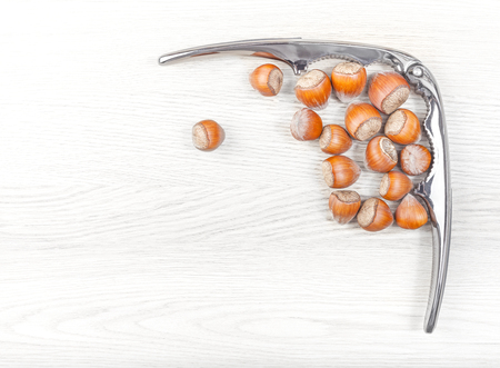 Hazelnuts and nutcracker on a white wooden background, space for text.の写真素材