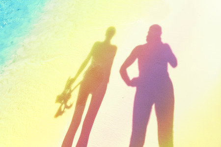 Stylized silhouettes of woman holding snorkeling equipment and man on the beach.の写真素材