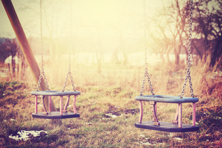 Vintage stylized two neglected empty swings, shallow depth of field.