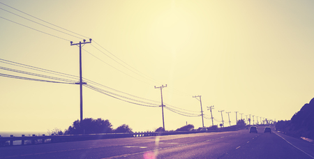 Vintage toned highway at sunset, picture against sun with lens flare, California, USA.