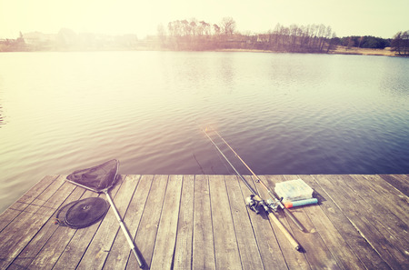 Vintage toned fishing equipment on a wooden pier at sunset.の写真素材