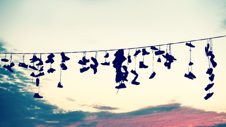 Retro stylized silhouettes of shoes hanging on cable at sunset, teenage rebellion concept.の写真素材