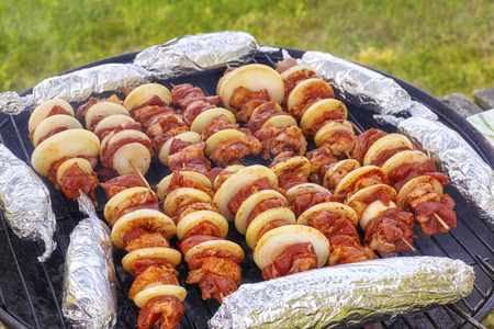 Close up picture of meat skewers with onions and corn cobs in aluminum foil, garden barbecue, selective focus.の写真素材