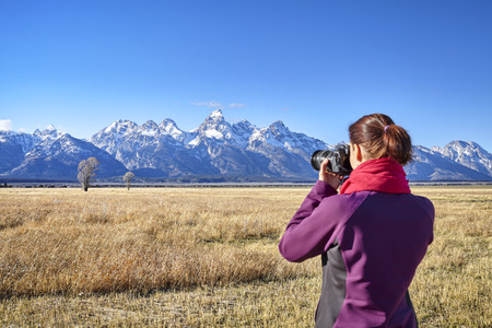 Rear view of a blurred woman taking pictures with DSLR camera in the Grand Teton National Park, focus on background, Wyoming, USA.の写真素材
