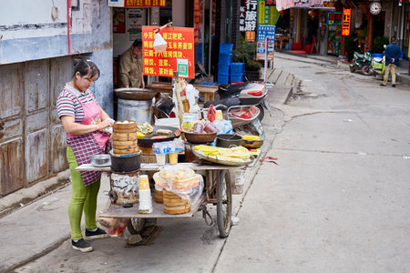 Lijiang, Yunnan, China - September 27, 2017: Woman prepares and sells breakfast food from street stall. Payment via QR code becomes very common in China.のeditorial素材