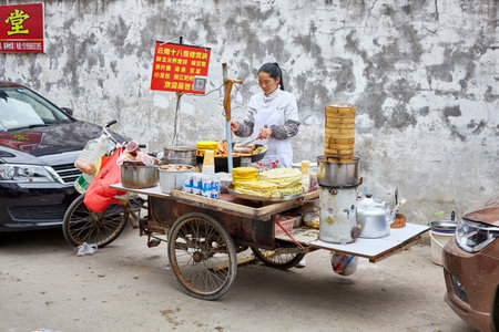 Lijiang, Yunnan, China - September 27, 2017: Woman prepares and sells breakfast food from street stall. Payment via QR code becomes very common in China.のeditorial素材