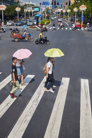 Guilin, China - September 15, 2017: Women with sun umbrellas cross street in downtown Guilin.のeditorial素材