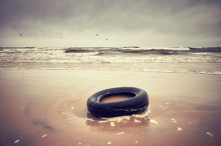 Old black rubber tire left on a beach, environment pollution concept, selective focus, color toned picture.                            の写真素材