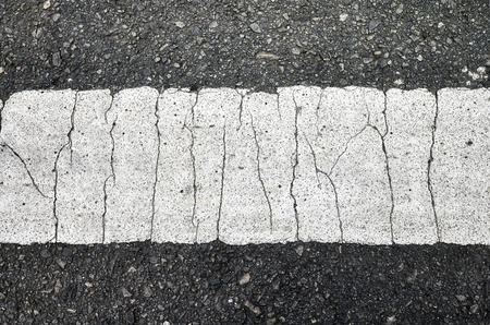 Close up picture of an asphalt road with a cracked white lane marking.の写真素材