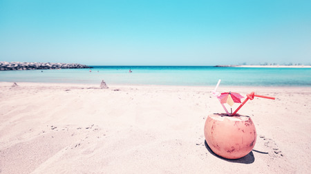 Retro toned wide angle picture of a coconut with two straws and colorful umbrella on a beach, summer holiday concept, selective focus.の写真素材