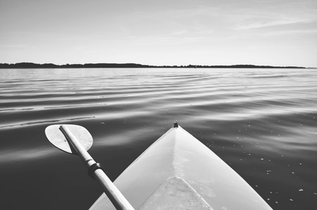 Retro stylized picture of a bow of a kayak with paddle on a lake, selective focus.