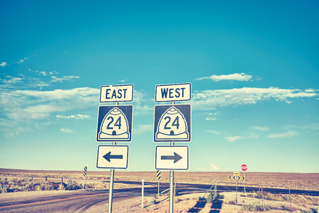 East or West, retro toned photo of road signs at sunset, choice and travel concept.の写真素材