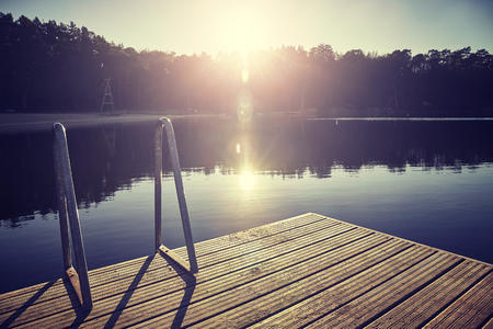 Vintage toned picture of a swimming platform at sunset with lens flare, selective focus.の写真素材