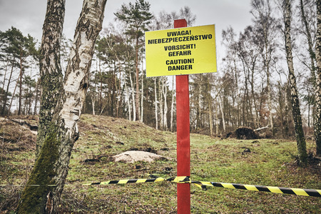 Located in a forest caution danger sign in Polish, German and English, color toned picture, selective focus.の写真素材