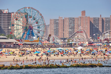 New York, USA - July 02, 2018: Crowded Coney Island beach and amusement park on a warm, hazy day.