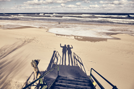 Silhouettes of a couple waving on a beach, color toning applied.