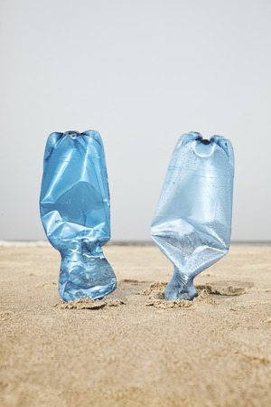 Two plastic bottles stuck in sand on a beach, selective focus, color toning applied.の写真素材