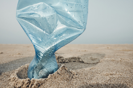 Close up picture of a plastic bottle stuck in sand on a beach, selective focus, color toning applied.の写真素材