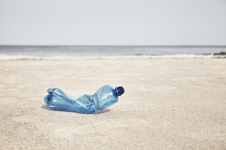 Empty plastic bottle on a beach, selective focus, color toning applied.