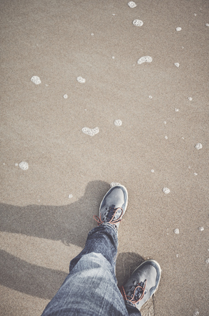 Standing on sand, top view of legs and shoes, color toning applied.の写真素材