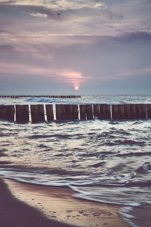 Wooden sea breakwater at sunset, color toning applied, long exposure with focus on groin.の写真素材