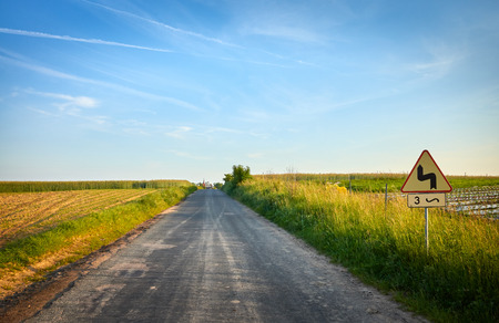 Picture of a country road with dangerous bends traffic sign at sunset.の写真素材