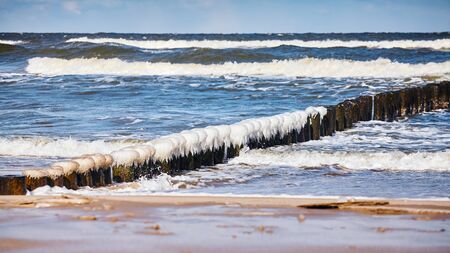 Beach with an icy wooden breakwater on a sunny day.の写真素材