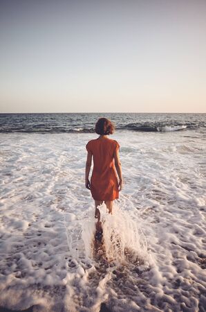 Rear view of a woman standing still in the ocean at sunset, color toning applied.の写真素材