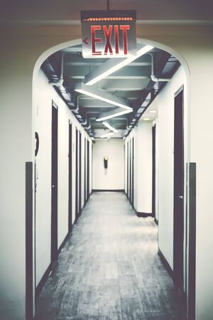 Emergency exit sign in empty corridor, selective focus, color toning applied.