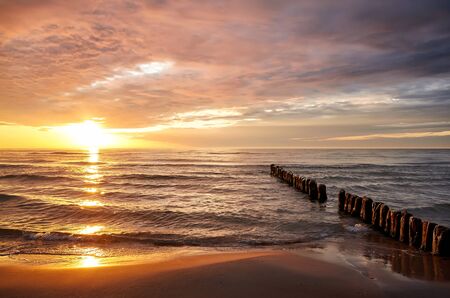 Beach with an old breakwater at beautiful sunset over sea.の写真素材