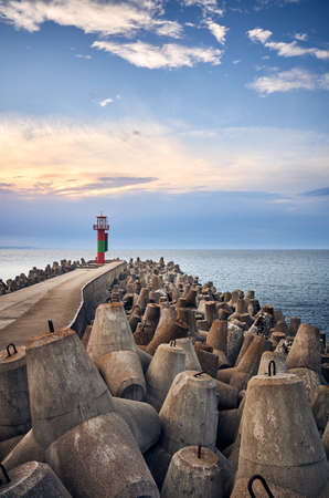 Pier with lighthouse protected by concrete breakwater tetrapods at sunset, Swinoujscie, Poland.の写真素材