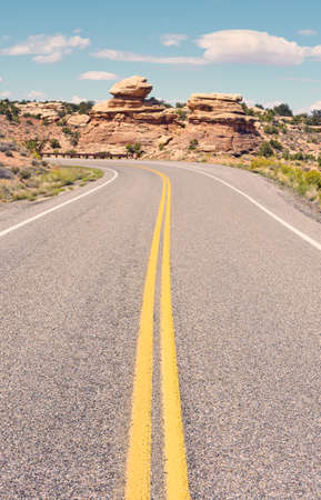 Retro toned picture of an empty road in Canyonlands National Park, focus on foreground asphalt, Utah, USA.の写真素材