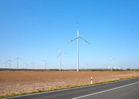 Picture of a wind turbine farm by a road against the blue sky.