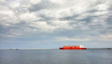 Red LNG tanker in port with stormy cloudscape.の写真素材