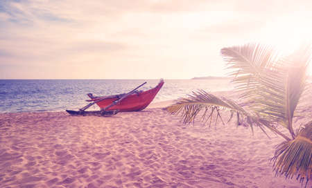 Small boat on an empty beach at sunset, color toning applied, Sri Lanka.の写真素材